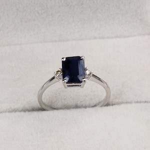 May include: A silver ring with a dark blue emerald-cut gemstone and two smaller diamonds on the side.