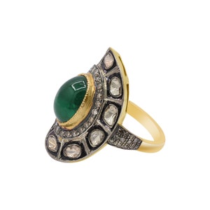 May include: A gold ring featuring a large green gemstone surrounded by smaller diamonds. The ring has a distinctive design with a fan-shaped setting.