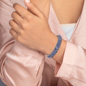 May include: A silver bangle bracelet with a row of light purple square-shaped stones.
