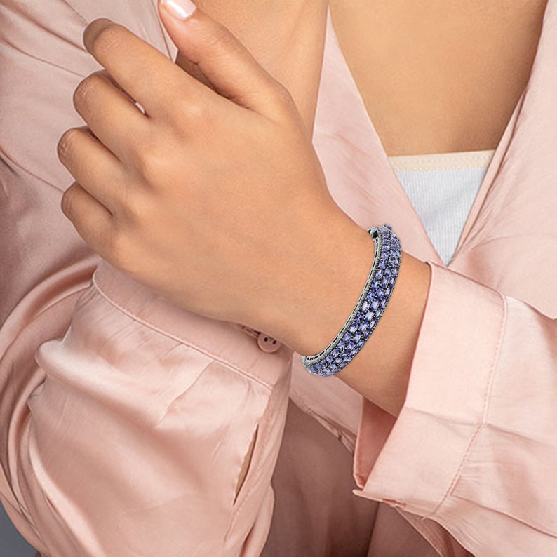 May include: A silver bangle bracelet with a row of light purple square-shaped stones.