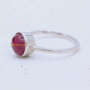 Puede incluir: Un anillo de plata con una piedra preciosa roja engastada en un engaste de bisel. El anillo es simple y elegante.