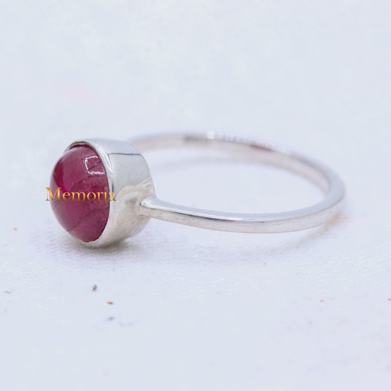 Puede incluir: Un anillo de plata con una piedra preciosa roja engastada en un engaste de bisel. El anillo es simple y elegante.
