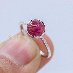 Puede incluir: Un anillo de plata con una piedra preciosa rosa engastada en un engaste de bisel. El anillo es simple y elegante.