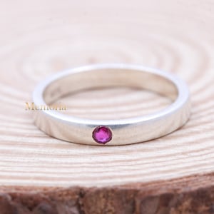 May include: A silver band ring with a single, small, pink gemstone set in the center.