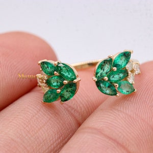 以下が含まれることがあります： エメラルドとダイヤモンドの宝石が2つのクラスターになった、分割デザインのゴールドリング。リングは、マルキーズ型のエメラルドとラウンドブリリアントカットのダイヤモンドがセットされています。