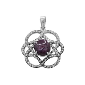 May include: A silver pendant featuring a dark red gemstone encircled by a ring of smaller white gemstones. The pendant is shaped like a flower with elaborate detailing.
