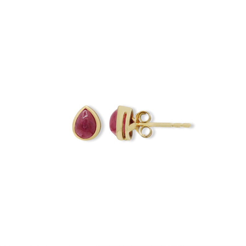 May include: A pair of stud earrings featuring teardrop-shaped, deep pink cabochon stones set in polished yellow gold bezels. One earring is shown from the front, while the other is viewed from the side, revealing the gold post and butterfly back.