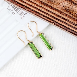 May include: A pair of gold earrings with green rectangular gemstones. The earrings have a simple, elegant design.