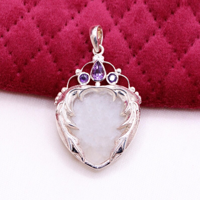 Peut inclure: Pendentif en argent avec un centre en pierre blanche en forme de c&oelig;ur. Le pendentif pr&eacute;sente un motif de couronne avec une pierre violette en forme de goutte et deux petites pierres violettes. Le pendentif a un cadre argent&eacute; orn&eacute; et d&eacute;coratif.