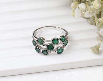 May include: A silver ring with multiple rows of round green gemstones.