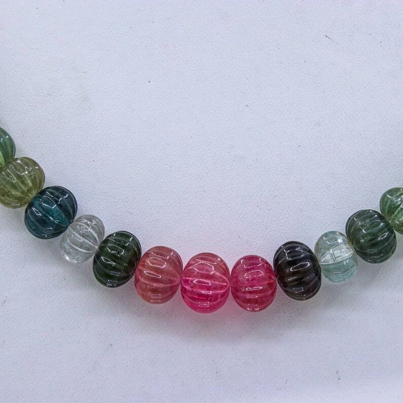 May include: A strand of multi-colored gemstone beads. The beads are round and have a ribbed texture. The colors of the beads are green, blue, pink, and red.