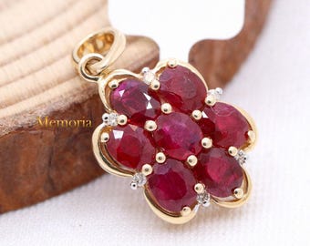 Puede incluir: Un colgante de oro con un diseño de flor que presenta nueve piedras de rubí rojo y pequeños diamantes. El colgante tiene un aro para sujetarlo a una cadena.