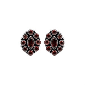 May include: A pair of silver earrings with red gemstone accents. The earrings feature a circular design with multiple small round stones and a larger oval-shaped stone in the center.