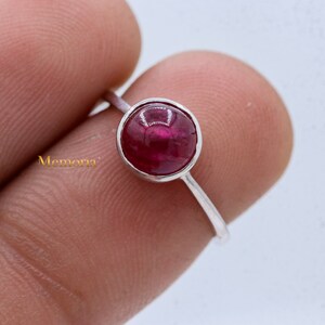 Puede incluir: Un anillo de plata con una piedra preciosa redonda de color rojo oscuro, tallada en cabuj&oacute;n.