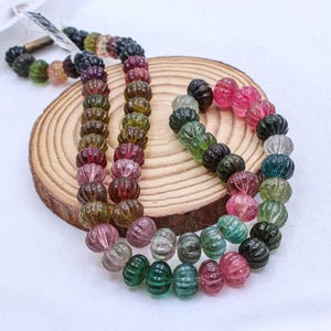 May include: A strand of multi-colored watermelon tourmaline beads. The beads are faceted and have a ribbed texture. The beads are strung on a clear elastic cord.