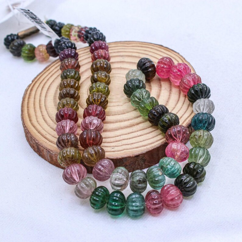 May include: A strand of multi-colored watermelon tourmaline beads. The beads are faceted and have a ribbed texture. The beads are strung on a clear elastic cord.