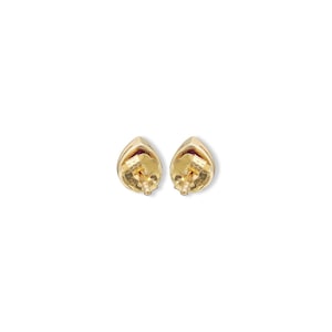 May include: A pair of gold stud earrings featuring a teardrop-shaped design with a deep red gemstone center. The back of each earring shows a gold post and a secure butterfly clutch mechanism, highlighting the metallic finish and construction.