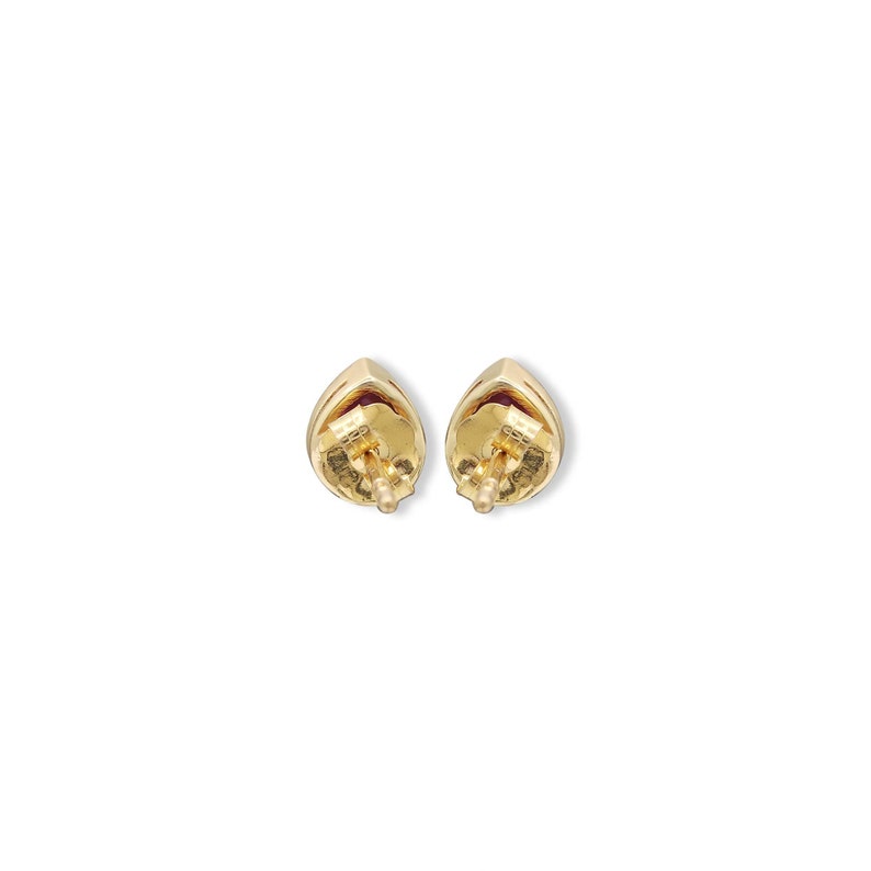 May include: A pair of gold stud earrings featuring a teardrop-shaped design with a deep red gemstone center. The back of each earring shows a gold post and a secure butterfly clutch mechanism, highlighting the metallic finish and construction.