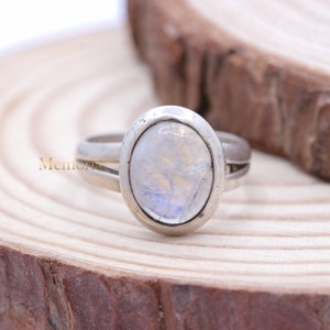 Peut inclure: Une bague en argent avec une grande pierre de lune ovale sertie dans un sertissage à bélière. La bague a une bande simple.
