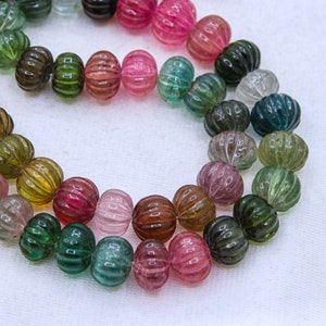 May include: A strand of multi-colored watermelon tourmaline beads. The beads are round and have a ribbed texture. The colors of the beads range from green to pink to red.