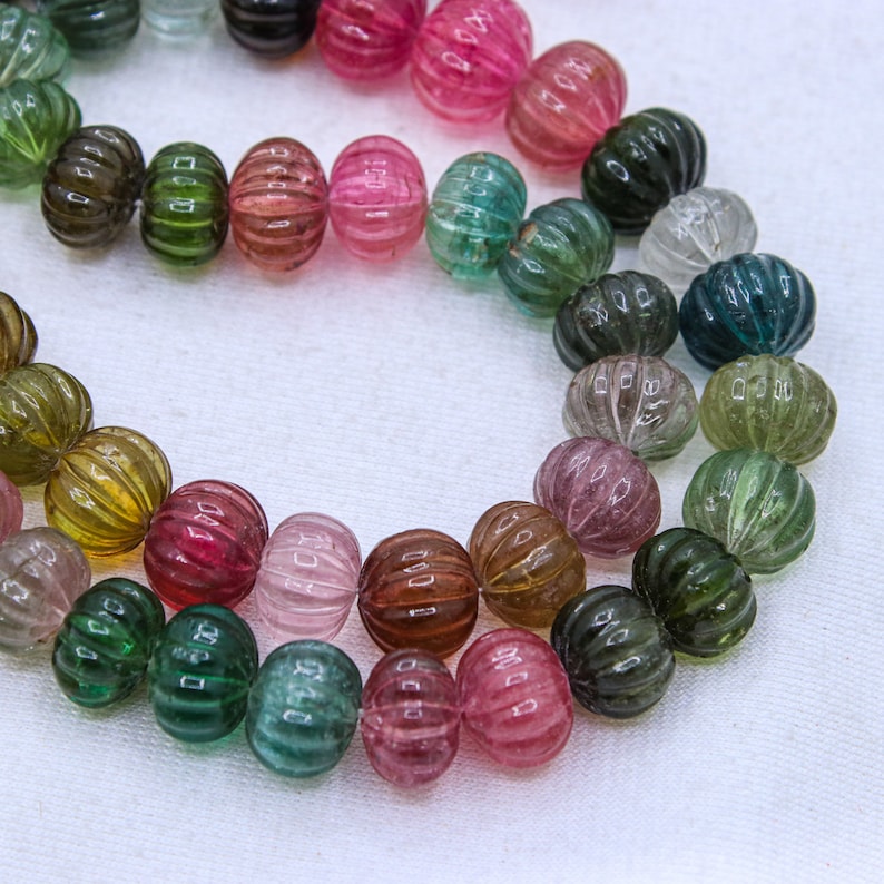 May include: A strand of multi-colored watermelon tourmaline beads. The beads are round and have a ribbed texture. The colors of the beads range from green to pink to red.