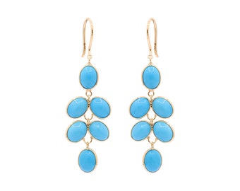 May include: A pair of gold-colored chandelier earrings featuring oval-shaped, light blue gemstones. Each earring has a hook and a cascade of gemstones, creating a dangling effect. The earrings are set against a white background.