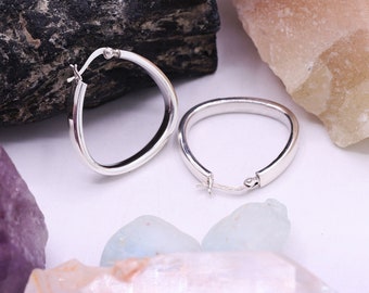 May include: A pair of silver hoop earrings. The earrings are oval shaped and have a smooth finish.
