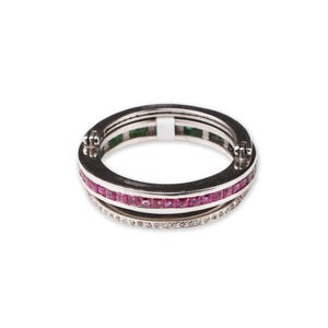 May include: A silver ring with three bands. The top band features small, square, pink gemstones. The middle band has green gemstones, and the bottom band is encrusted with small, clear gemstones. The ring is set against a white background.