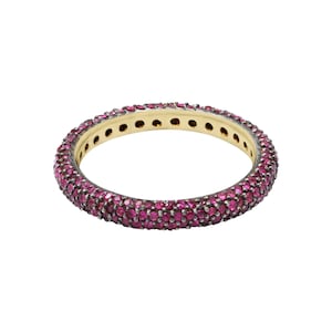 May include: A gold band ring with a row of small pink gemstones around the entire band.