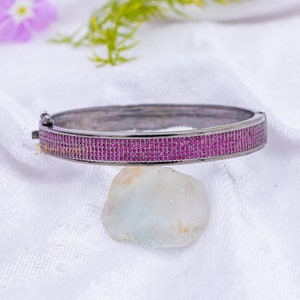 May include: A black bangle bracelet with a row of pink cubic zirconia stones.