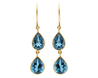Puede incluir: Un par de pendientes colgantes de oro, cada uno con dos piedras preciosas azules facetadas en forma de pera suspendidas verticalmente. Las piedras están engastadas en oro y cuelgan de finos ganchos, creando un diseño simétrico.