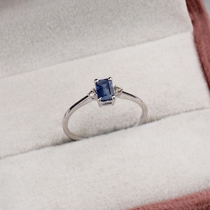 May include: A silver ring featuring a blue emerald-cut gemstone and two smaller diamonds on the band.