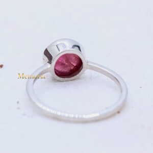 Puede incluir: Un anillo de plata con una piedra preciosa rosa engastada en un engaste de bisel. El anillo se muestra desde atr&aacute;s, revelando el engaste y la banda.