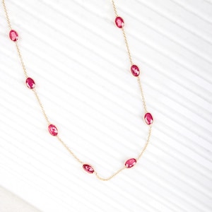 May include: A gold chain necklace with oval-shaped red gemstones. The necklace is on a white background.