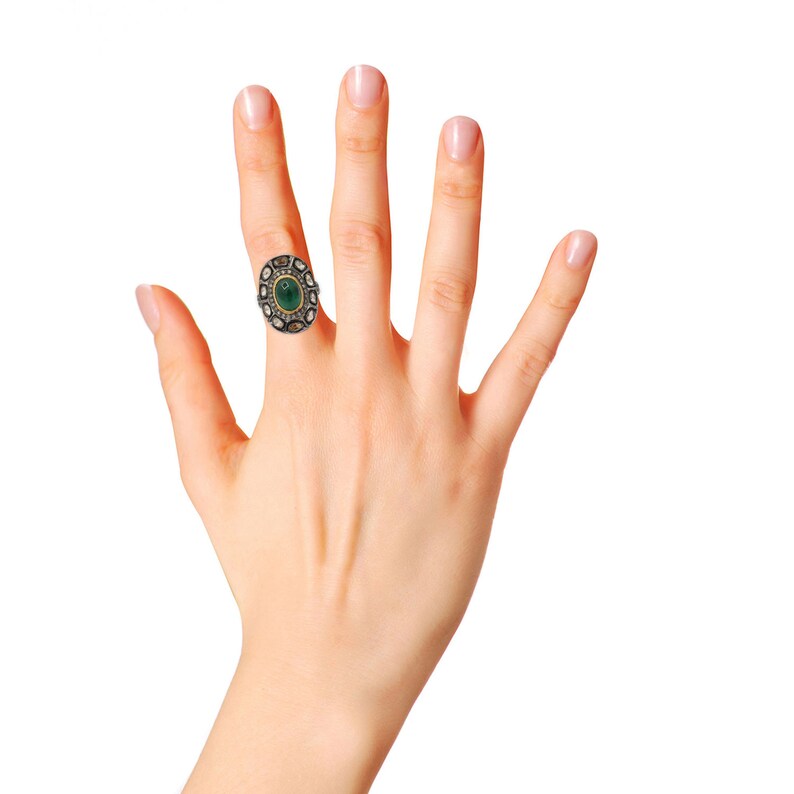 May include: A silver ring featuring a green oval gemstone surrounded by smaller diamonds. The ring is set in a gold band.