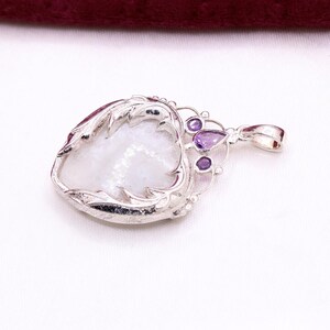Peut inclure: Pendentif en argent avec une pierre blanche iris&eacute;e en forme de c&oelig;ur, encadr&eacute;e d'une monture argent&eacute;e d&eacute;corative. Le pendentif comporte trois petites pierres pr&eacute;cieuses violettes et une boucle pour une cha&icirc;ne. Design orn&eacute; et &eacute;l&eacute;gant.