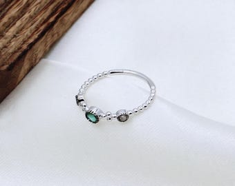 May include: A silver ring with a beaded band and three small stones. The stones are green, clear, and black.