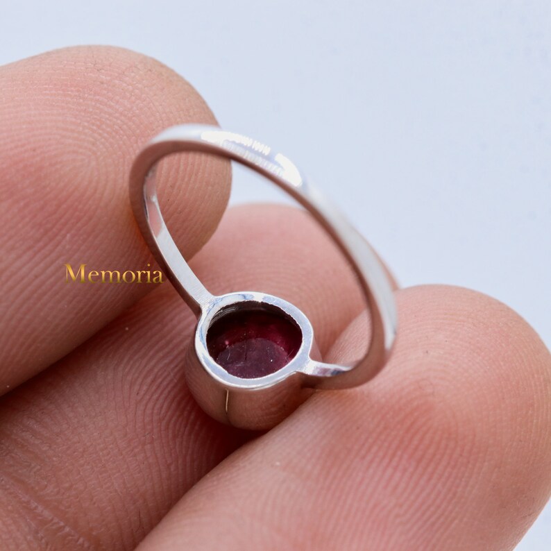 Puede incluir: Un anillo de plata con una piedra preciosa redonda de color rojo oscuro engastada en bisel.