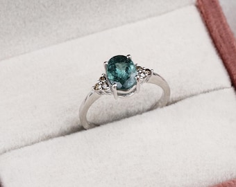 May include: A silver ring with a large oval-shaped green gemstone surrounded by smaller white gemstones.
