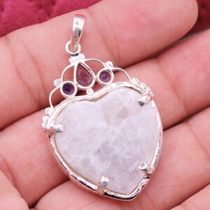 Peut inclure: Pendentif en forme de c&oelig;ur avec un cadre argent&eacute;. Le pendentif pr&eacute;sente une grosse pierre claire au centre, avec de plus petites pierres violettes et rouges en haut. Le pendentif est orn&eacute; d'un &eacute;l&eacute;ment d&eacute;coratif en forme de couronne.