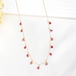 May include: A gold chain necklace with dangling red teardrop-shaped gemstones.