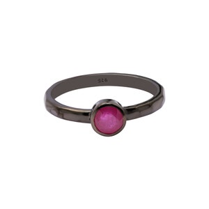 Può includere: Un anello in argento ossidato nero con una pietra preziosa rosa. L'anello è timbrato con il numero "925".