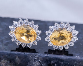 May include: A pair of silver earrings with a yellow oval gemstone surrounded by a halo of smaller clear gemstones.