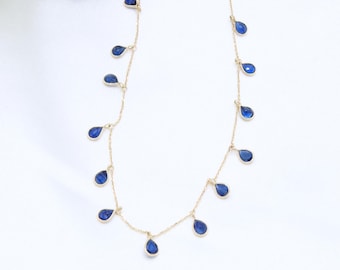 May include: A gold chain necklace with multiple teardrop-shaped blue gemstones dangling from it.