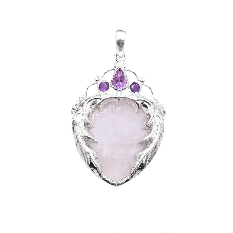 Peut inclure: Pendentif argent&eacute; avec une pierre rose p&acirc;le en forme de c&oelig;ur. Le pendentif pr&eacute;sente un motif de couronne avec trois pierres pr&eacute;cieuses violettes. Le c&oelig;ur est encadr&eacute; d'une bordure orn&eacute;e et poss&egrave;de une boucle pour une cha&icirc;ne.