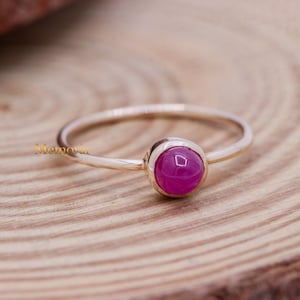 May include: A delicate gold ring with a single, round, pink gemstone set in a bezel setting.