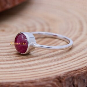 Puede incluir: Un anillo de plata con una piedra preciosa redonda de color rojo oscuro, tallada en cabuj&oacute;n. El anillo es simple y elegante.