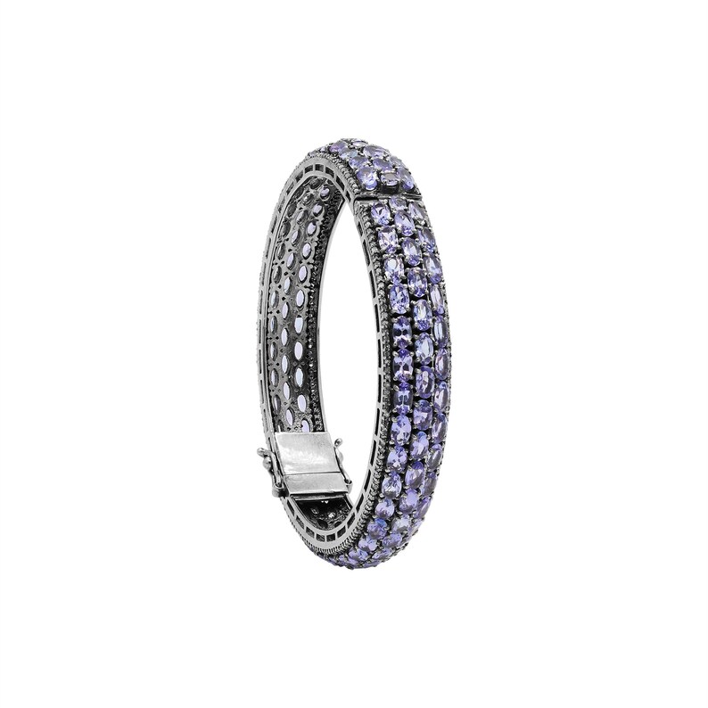 May include: A silver bangle bracelet with a row of light purple gemstones around the entire circumference.