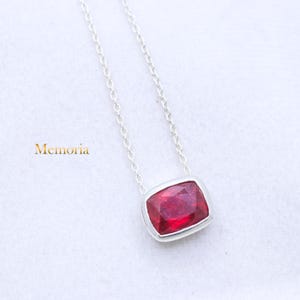 May include: A silver chain necklace with a red gemstone pendant. The pendant is a rectangular shape with a beveled edge.