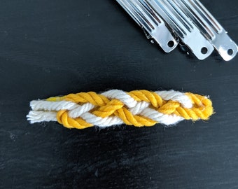 Pode incluir: Três grampos de cabelo prateados e um elástico de cabelo trançado de corda amarela e branca.